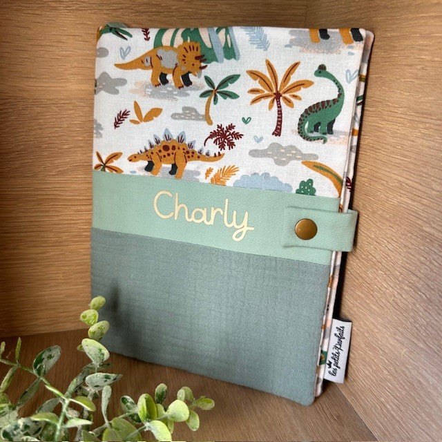 Protège carnet de santé sur le thème des dinosaures personnalisé avec le prénom Charly en doré chez Les petits parfaits