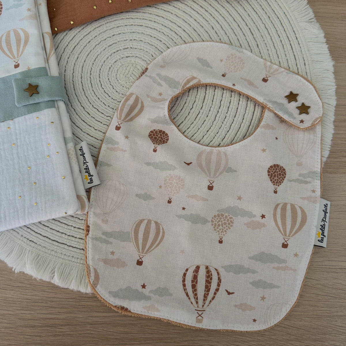 bavoir bébé évolutif imprimé montgolfières grâce à ces 2 boutons pressions en forme d'étoile dorée. Le dos du bavoir naissance est en éponge biologique.