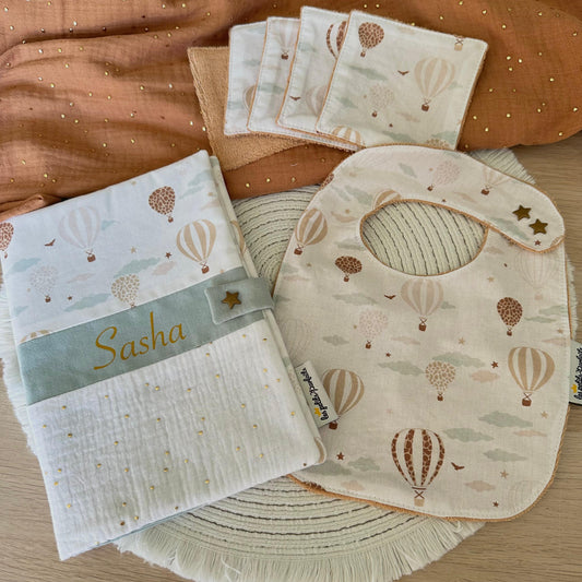 Coffret naissance bébé univers montgolfières composé d'un protège carnet de santé personnalisé avec prénom (police et coloris au choix), d'un bavoir bébé évolutif double pression étoile en éponge bio et de 5 lingettes lavables zéro déchet.